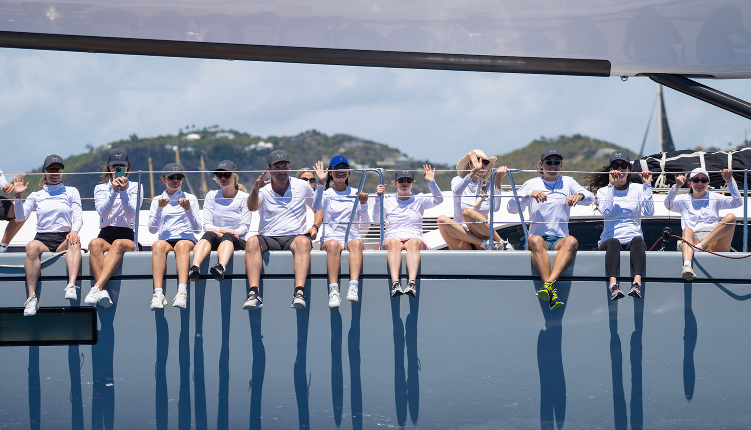 A racing crew waves from the rail during racing at the 2025 Bucket Regatta, by Martin Baum.