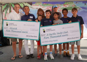 Photograph of Thursday’s 2025 St Barths Bucket Skippers’ Meeting where checks for 5,000 euros were presented to youth sailing members from the St. Barths Yacht Club and Ernest Brin, Directeur du Port here and head of the Foundation for Emergency Medical Equipment (FEMUR).