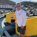 Photograph of MarkSetBot’s Jim Thompson standing next to two robotic markers, at the 2026 St Barths Bucket Regatta.